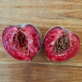 An Indian Blood peach cut in half on a wooden board, with bright red flesh and the stone still stuck in one half